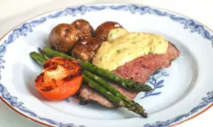 En tallrik med ryggbiff, potatis, sparris och tomat. En krämig sås toppar köttet. Ett perfekt ryggbiff recept!