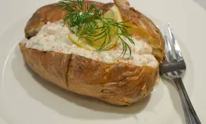 En saftig bakad potatis fylld med en krämig röra med rom, dill och citron. En gaffel ligger bredvid.