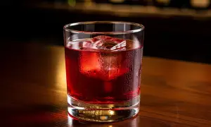 Ett glas med en röd negroni, isbitar och kondens på glaset, på en träyta. Perfekt för ett negroni recept.