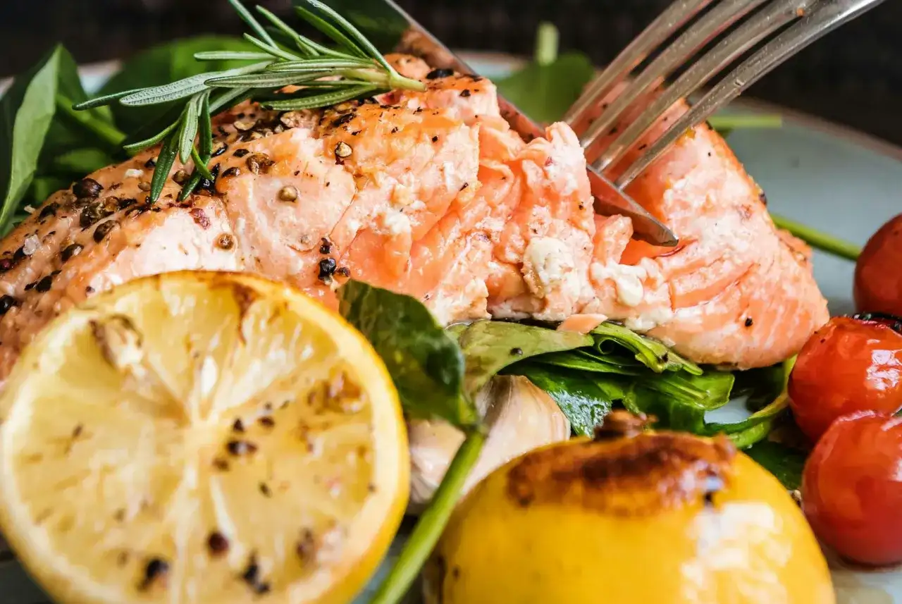 En saftig bit lax i ugn, kryddad med peppar och örter, serveras med citron, körsbärstomater och gröna blad.