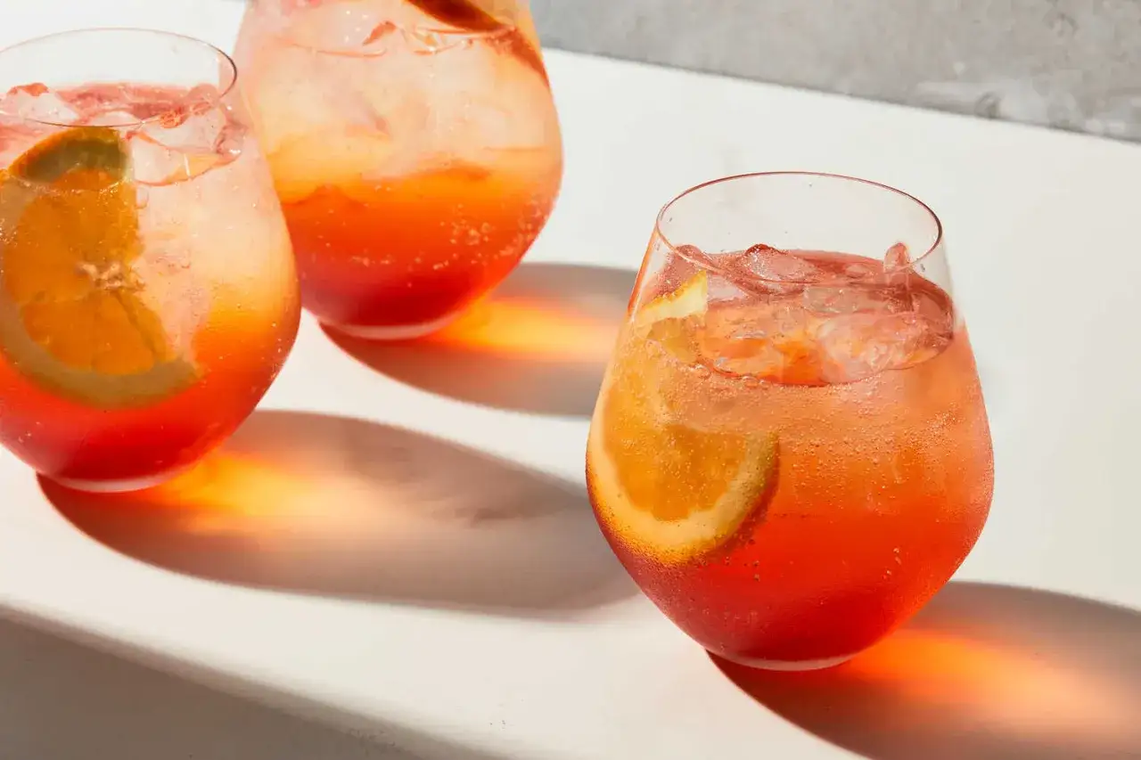 Tre glas med Aperol Spritz, fyllda med is och apelsinskivor, kastar varma skuggor.