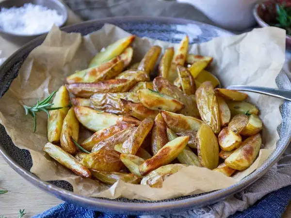 Klyftpotatis i airfryer, gyllene och krispiga, serverade med färsk rosmarin. Perfekt tillbehör!